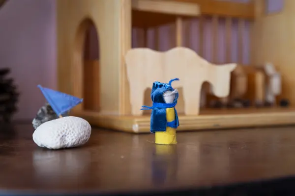 Omino blu con bandierina davanti a una stalla in legno